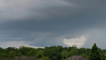 Dark, swirling clouds forming over an area with green trees. The ominous clouds suggest a possible severe storm approaching.